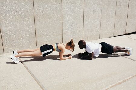Two professional athletes of different nationalities do a plank exercise outdoors in the fresh air.