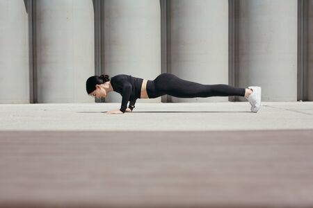 Fitness trainer doing morning push-up exercises on the street in park on the promenade against the...
