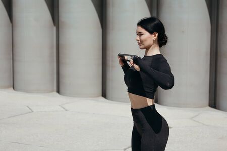 Profile of Asian woman doing pectoral muscle exercises with rubber sports tape in hands on the street in the parkの写真素材