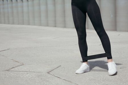 Close-up of legs of a Pilates trainer doing exercises on back muscles of the legs with a sports tape on the ankles on the streetの写真素材