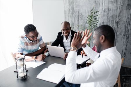 Lively discussion by dark-skinned colleagues holding a morning meeting in the office to discuss working issuesの写真素材