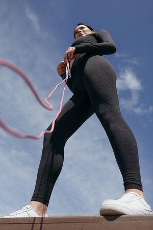 Bottom view on the girl trainer with a rope in hands on sky background. Morning sports shooting.の写真素材