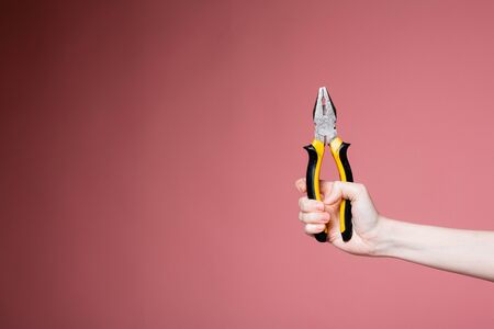 Female hand on a pink background in the studio holds pliers as an advertising banner for a construction store and servicesの写真素材