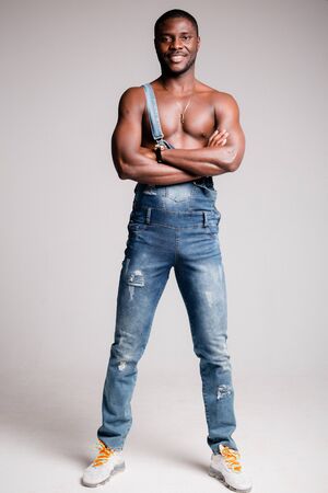 Dark-skinned African-American man with naked torso in denim pants with suspenders crossed his arms on his chest.の写真素材