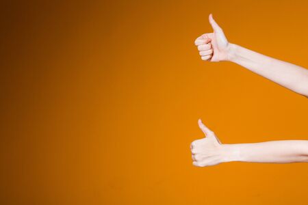 Female hands showing thumbs up in approval on an orange background. Slender female hands showing sign like.の写真素材