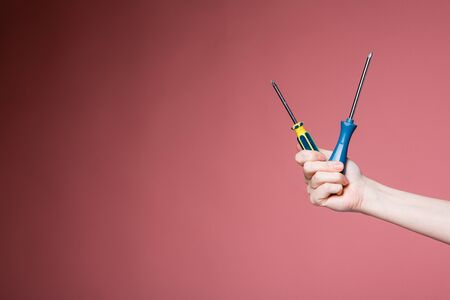 Female hand on a pink background holds two screwdrivers. Advertising banner for construction stores.の写真素材