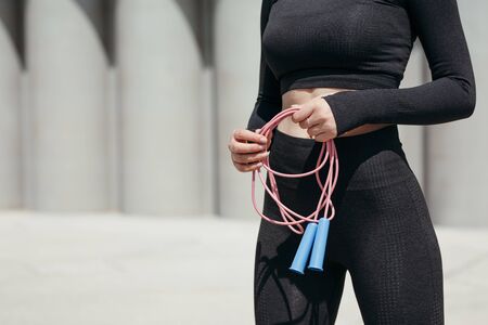 Close-up of a girl in a tight-fitting tracksuit holding a rope in her hands while preparing for...