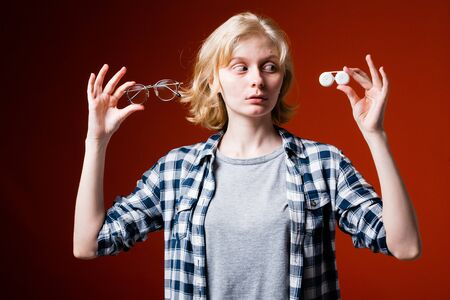 Blonde girl holds the glasses and contact lenses and making the choice to lenses. Attractive girl on...