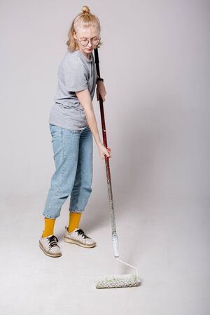 Girl paint the floor with white paint during a routine repair in photo Studio. Professional worker painter spends a facelift.の写真素材