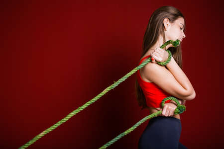 profile of a girl with long hair who is tormentedly holding two green ropes which mean personal problems, loans and debts on a burgundy background.の写真素材