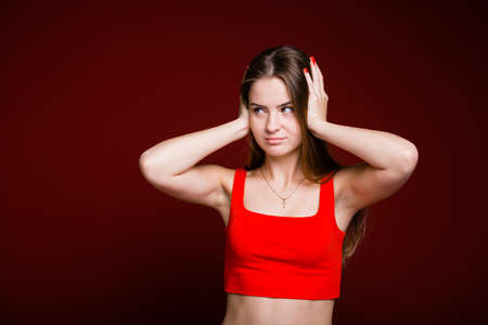 A young girl with long hair and a red T-shirt covered her ears with her hands and looks maliciously...