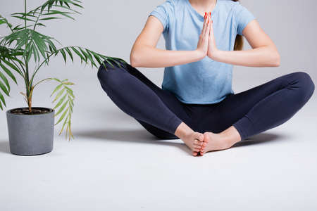 Close-up of portrait of yoga trainer girl sitting in lotus position on a white background next to a green flowerの写真素材