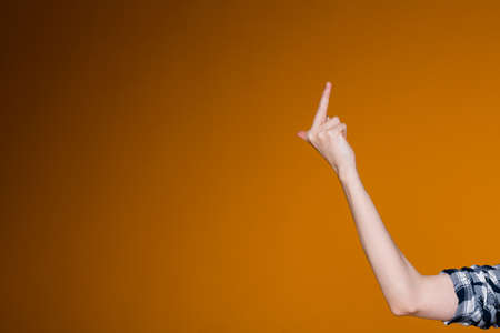 Female hand shows the middle finger on the right of the screen on an orange background. The concept of indecent and defiant gesturesの写真素材