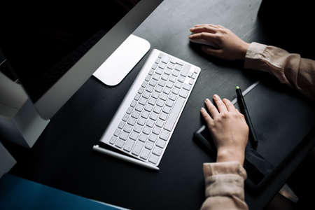 Close-up of a girl behind a Desk. A freelancer works on a laptop using keyboard and graphics tablet.