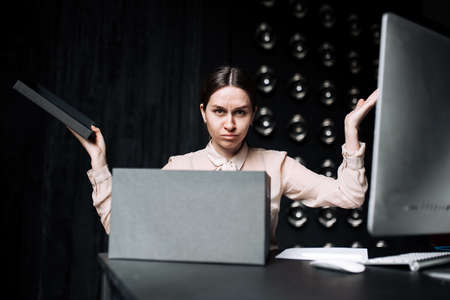 A confused worker is not able to find a solution. Woman sitting at office Desk with a computer and a folder for documents.の写真素材