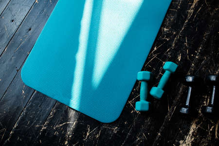 Sport blue Mat for sports lies near the dumbbells on the wooden dark floor with a light textureの写真素材