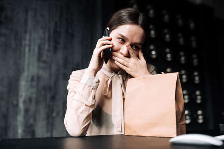 A girl in a beige blouse covers her mouth from overwhelming emotions and thanks the phone for the giftの写真素材