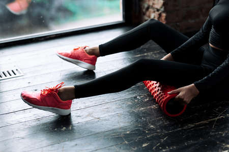 Close-up of legs in black leggings of a girl who placed a massage roll under her hind muscles to work through the fascia.の写真素材