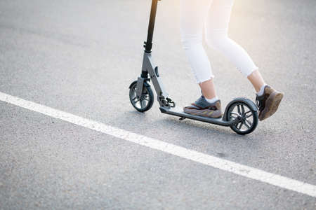 Closeup of the bottom of a scooter and legs of a girl who is riding down the street on acquired...