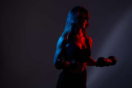 Portrait of a boxer girl who stands in a neon red light with dumbbells in her handsの写真素材