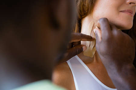 An African American man glues tape on a girls neck. Patch for face correction and wrinkle preventionの写真素材