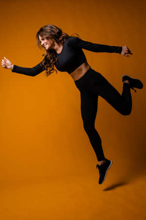Caucasian girl of athletic physique makes a jump on an orange background. Happy fitness trainer in jump, movementの写真素材