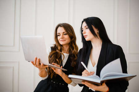Two women business partners are standing with a laptop and documents in their hands. Sales growth...