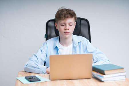 Coronavirus quarantine training. Cute caucasian boy is writing in a notebook during an online lesson.の写真素材