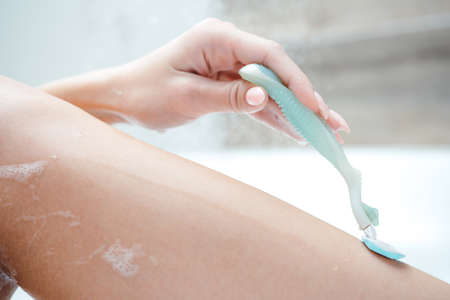 Close-up of a female leg. Woman shaves her legs with a razor while lying in a bubble bathの写真素材