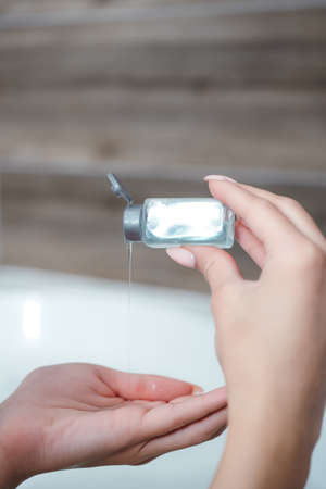 Close-up of female hands with shower gel. Girl pours blue shower gel into the palm while sitting in...