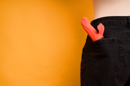 Bright dildo in the back pocket of jeans. Photo of a woman from behind. The concept of sex toys for arousal. Space for textの写真素材