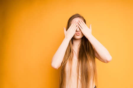girl covers her face with her hands, portrait on an orange backgroundの写真素材