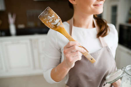 Close-up of a wooden spatula in flour for cooking in the hands of a cute girl