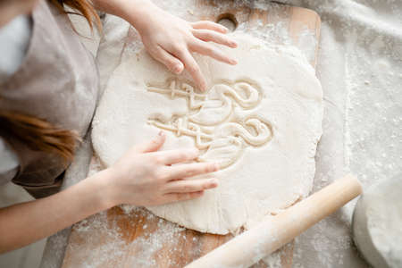 Hands draw patterns on dough with flour in the kitchen. Making cookies. Cooking