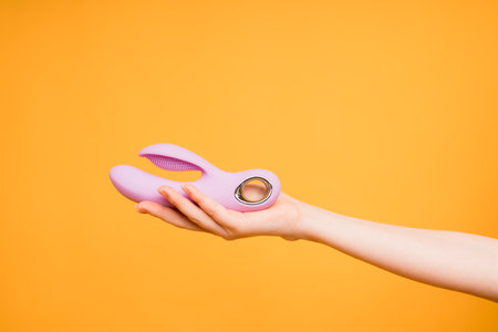 Pink sex toy in hand, present for adults, Saint Valentines Day, 8 March concept. Small dildo vibrator for women on yellow backgroundの写真素材