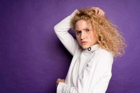 a curly-haired woman grimaces and pulls her hands against her face. gloomy emotions on a purple...