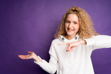 playful woman shows with her hands to the free space on the background for the inscription. curls on the headの写真素材