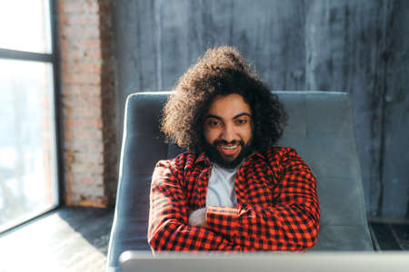 Smiling young egyptian sitting against the background of a large window and looking at a laptopの写真素材