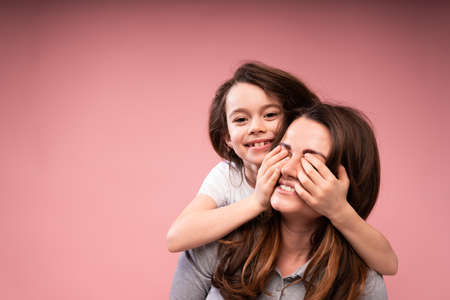 The smiling daughter looks at the cheerful mother and closes her eyes with her palms. Games with...