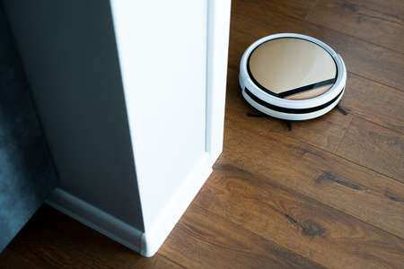 a robot vacuum cleaner cleans an apartment with a loft interior on a brown laminate. the view...