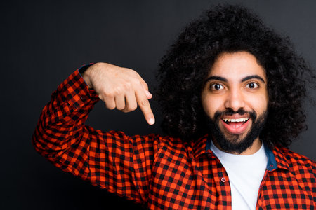 Handsome egyptian man in red plaid shirt pointing down with his index finger opening his mouthの写真素材