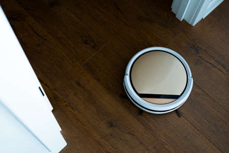 Photo from above. A remote-controlled vacuum cleaner moves across the parquet floorの写真素材