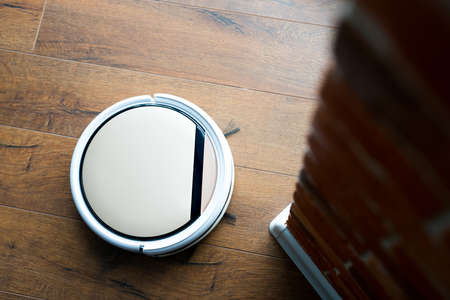 A remote-controlled vacuum cleaner vacuums laminate flooring near a brick wall. Modern technologiesの写真素材