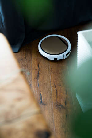 Light robot vacuum cleaner removes dust and dirt in an apartment on a wooden parquetの写真素材
