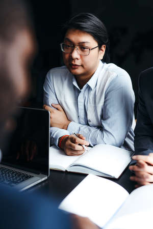 Young korean manager with glasses and a blue shirt sits at a table with a notebook at a meeting in the officeの写真素材