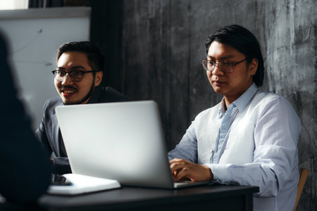 Two Vietnamese men in business suits and glasses are sitting in the office at a table with a laptop and conducting negotiations. Brainstorming concept, office workの写真素材