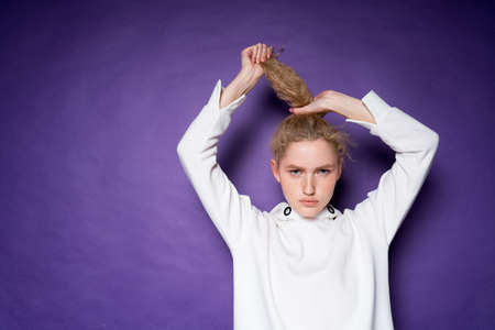 Attractive serious girl doing ponytail holding her curly blonde hair with her hands and lifting it upの写真素材