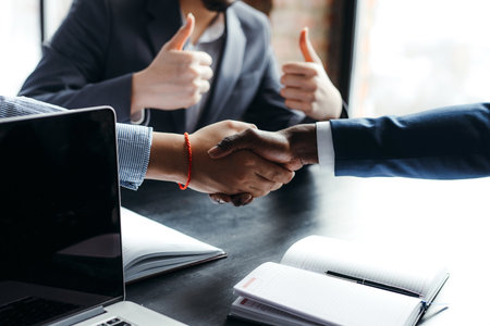 Businessmen shaking hands with each other against the background of an employee showing two thumbs...