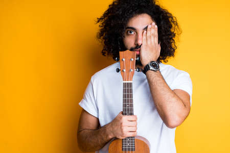 Handsome african american man holding a guitar in one hand and covering half of his face with his...