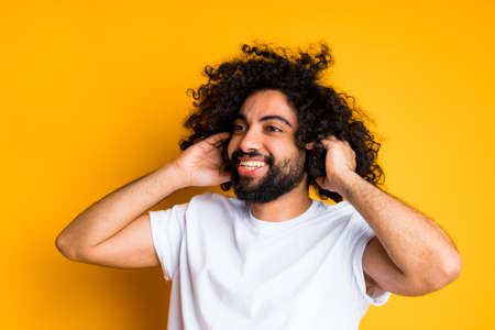 Cute cheerful african american guy listening to music laughing and holding headphones to his ears